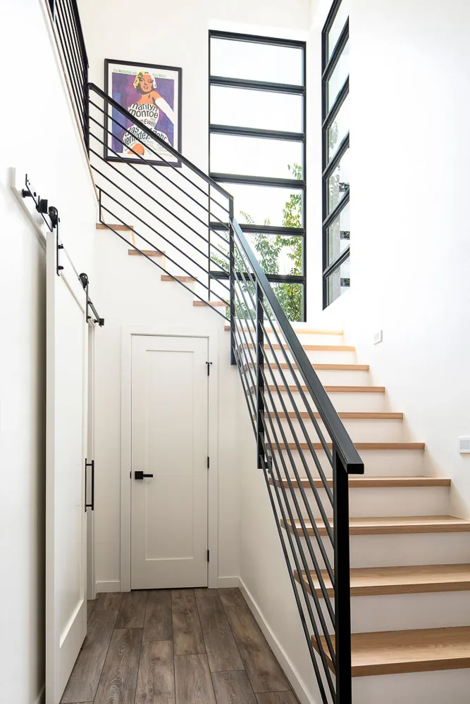 Modern interior stairwell featuring wood steps, black metal railing, and vertical rectangular windows providing natural light.