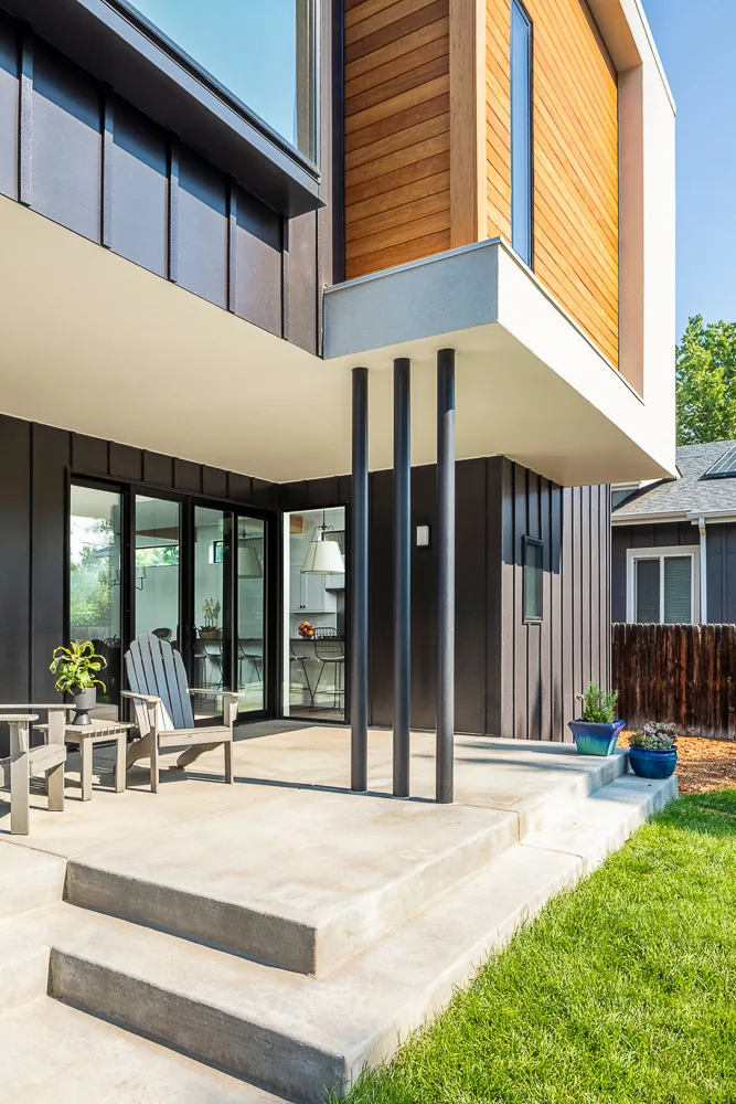 The Dempster Residence features a cantilevered volume with wood siding, black vertical metal siding, and a concrete patio with steps.