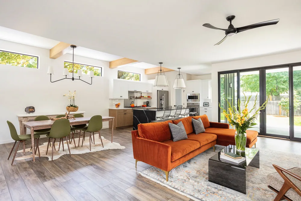 Open living and dining space with exposed wood beams, clerestory windows, and sliding black-framed glass doors to the outside.