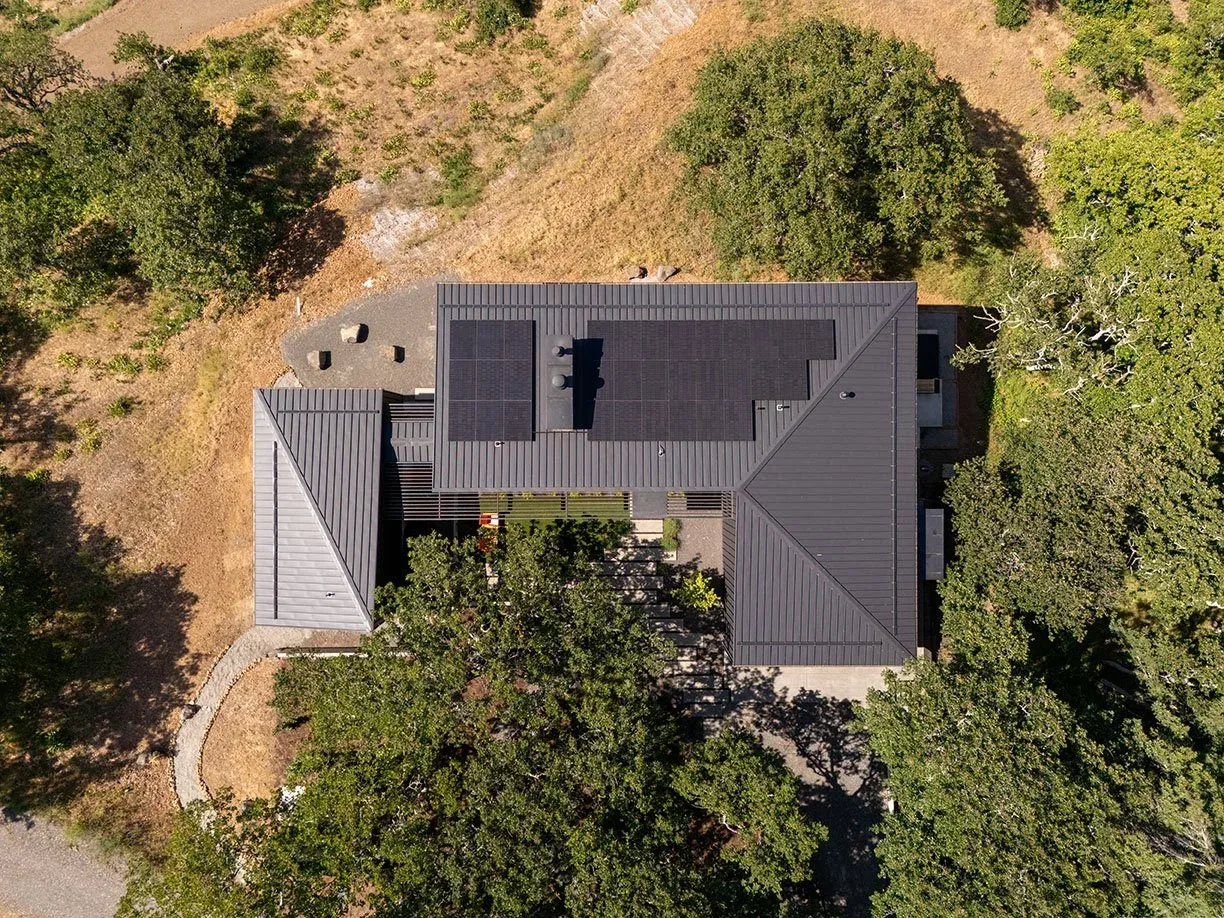 Hidden Oaks Residence with solar panels on a standing seam metal roof in a wooded, hillside site.