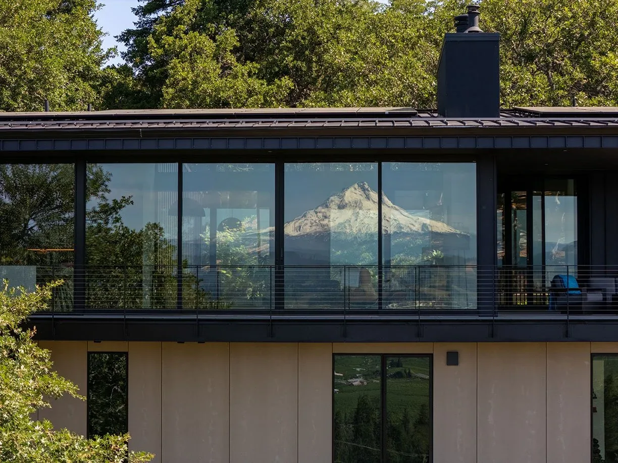 The Hidden Oaks Residence by Centerfield Studio features large floor-to-ceiling windows reflecting forest and mountain views.