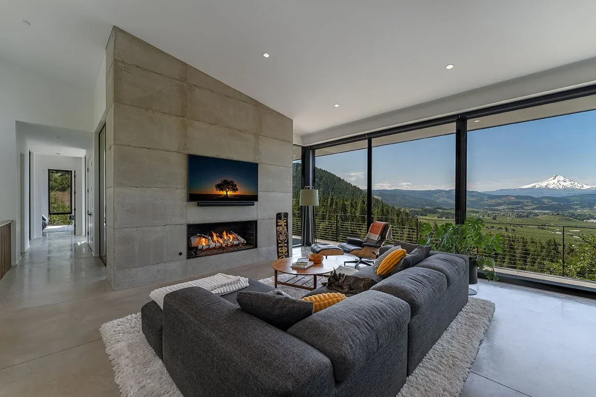The Hidden Oaks Residence living room features a concrete fireplace and expansive glazing framing mountain views.