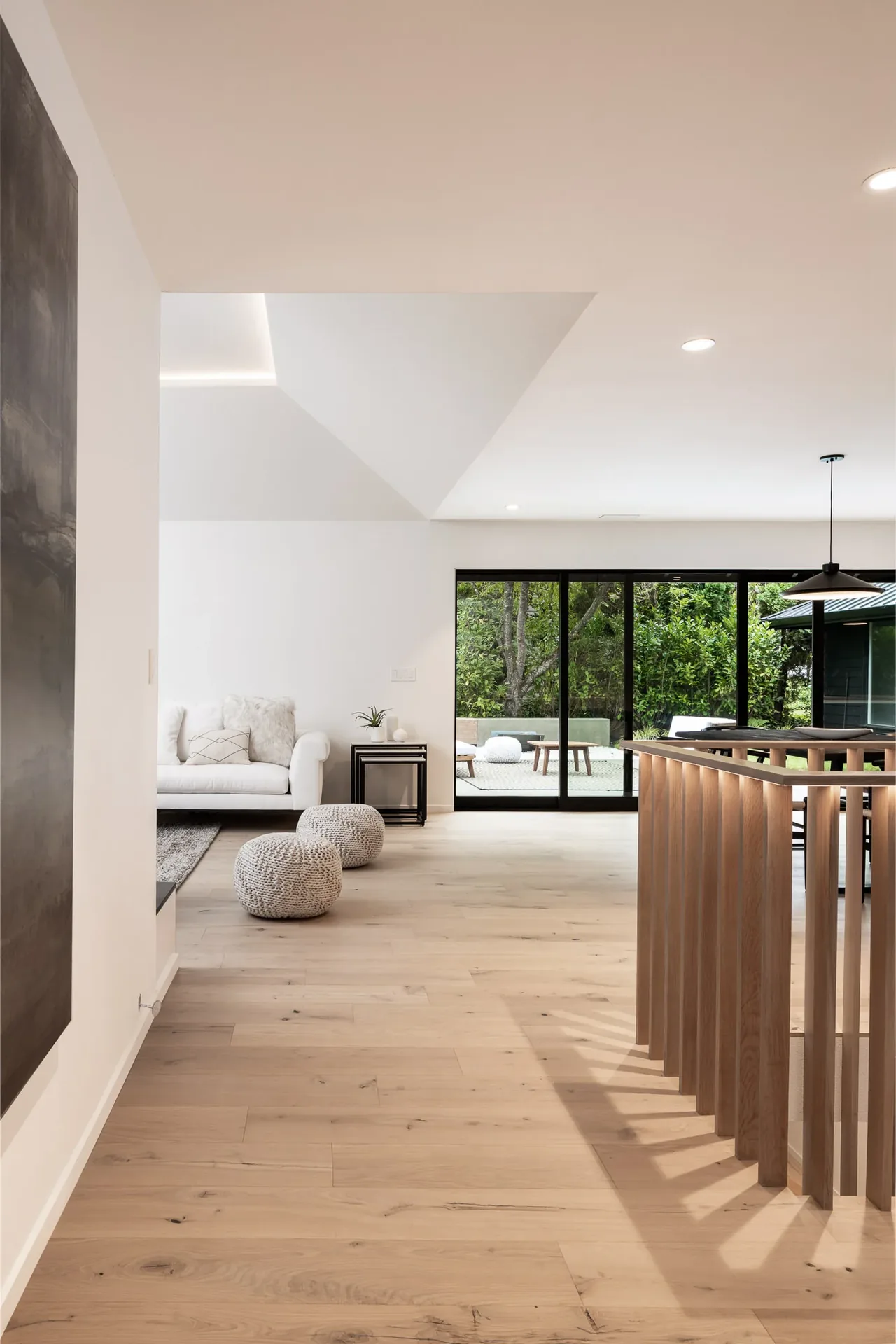 Open living space with wood flooring and floor-to-ceiling sliding glass doors overlooking a patio and garden.