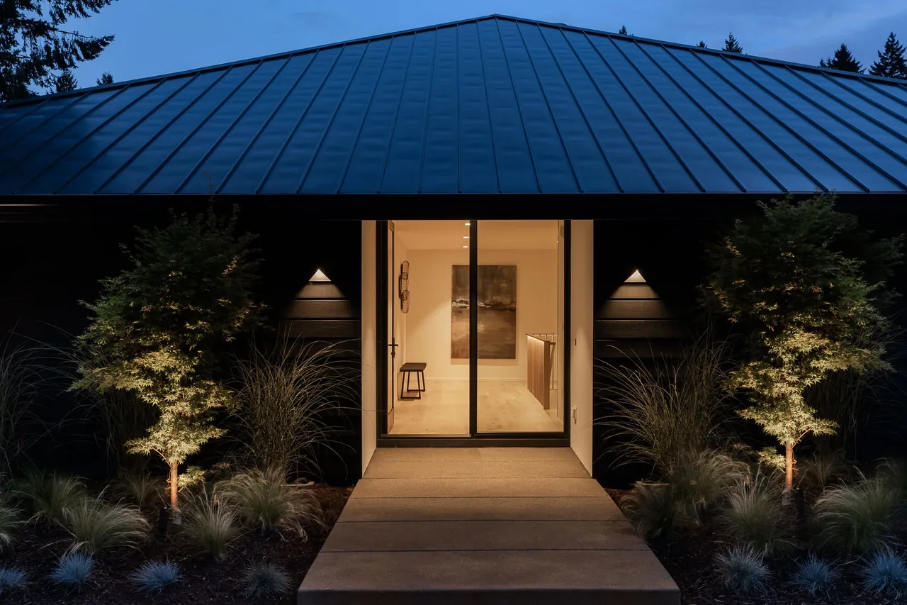 The Cardinal House features a metal roof, symmetrical outdoor landscaping, and an illuminated front pathway leading to a glass door entry.