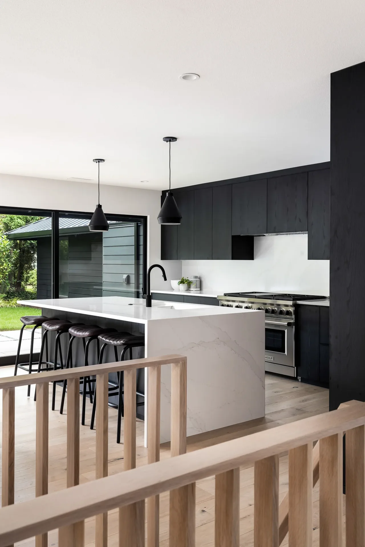 Kitchen in a modern home with black wood cabinets and a white marble island featuring bar stools and pendant lights.