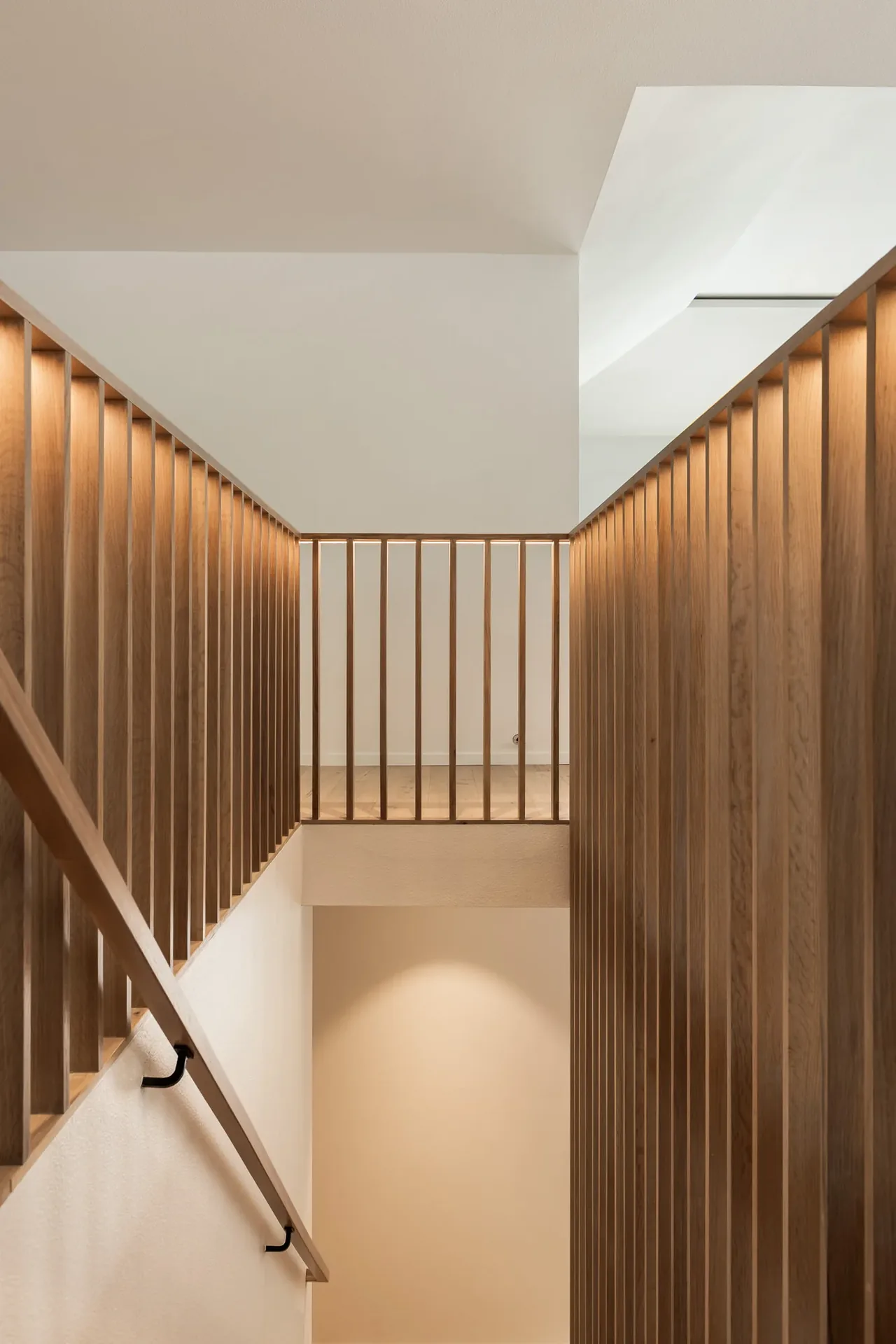 Light wood vertical slat stair railing defines the stairwell and landing area.