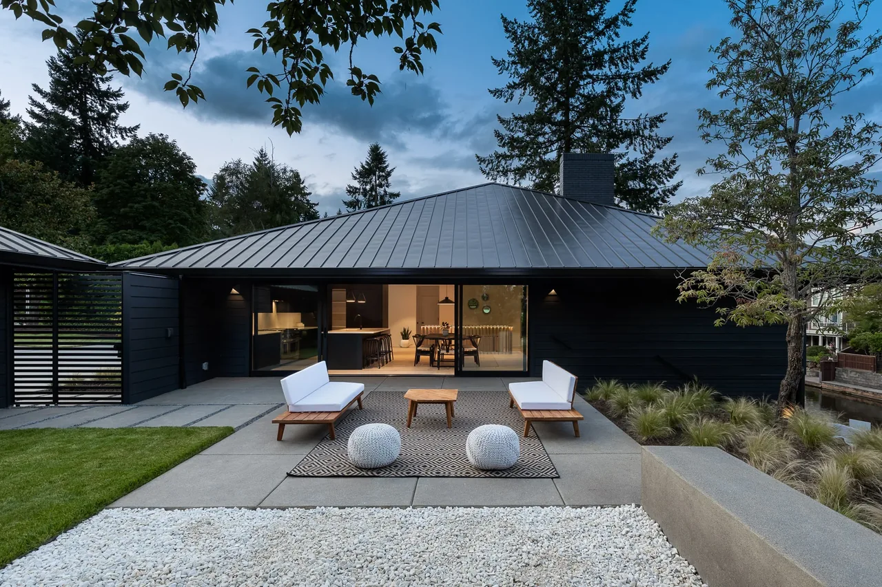 Modern house exterior rear view with shaded patio seating and sliding glass doors to the kitchen and dining area.