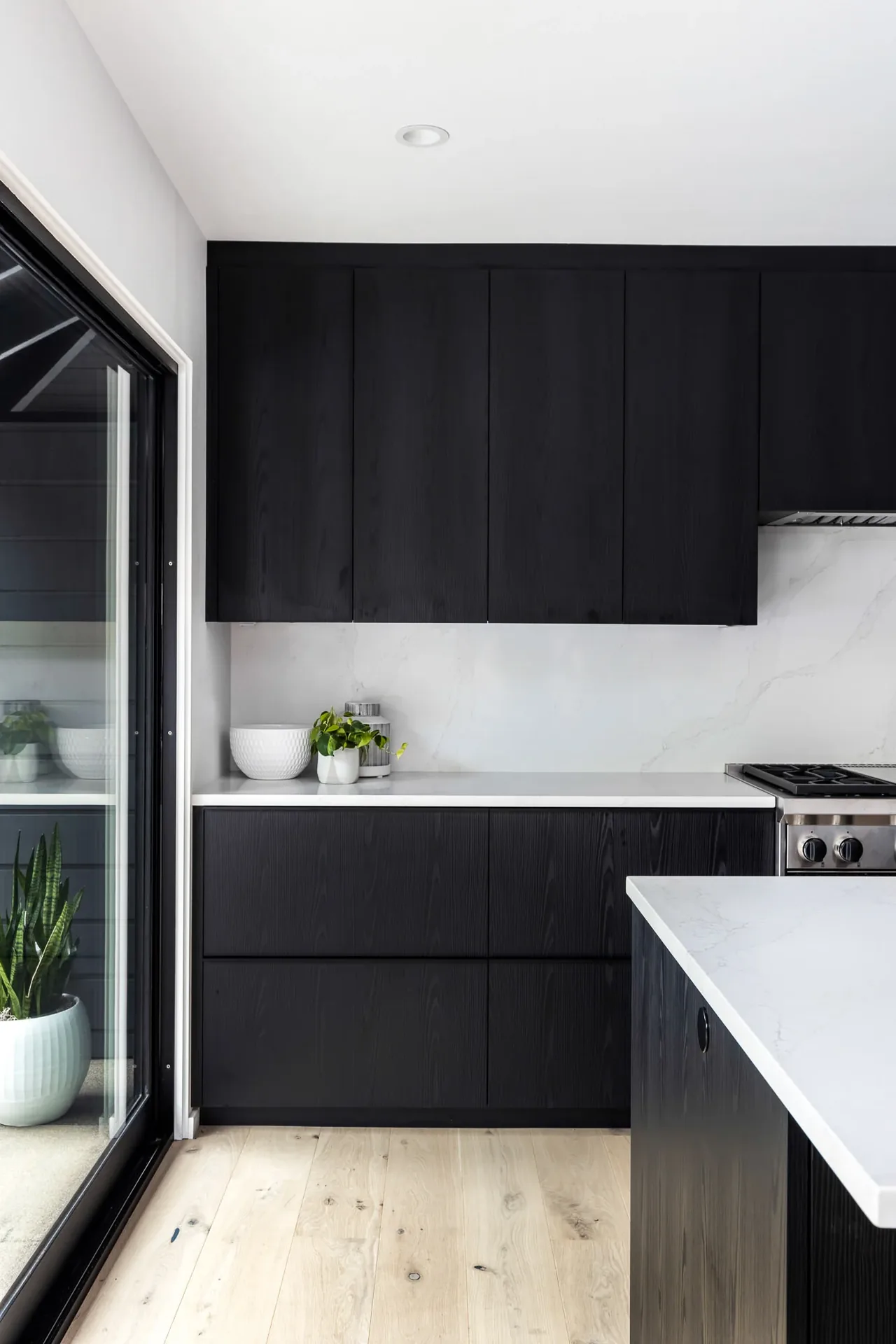 Kitchen interior featuring black wood cabinetry and a white marble countertop with a sliding glass door.