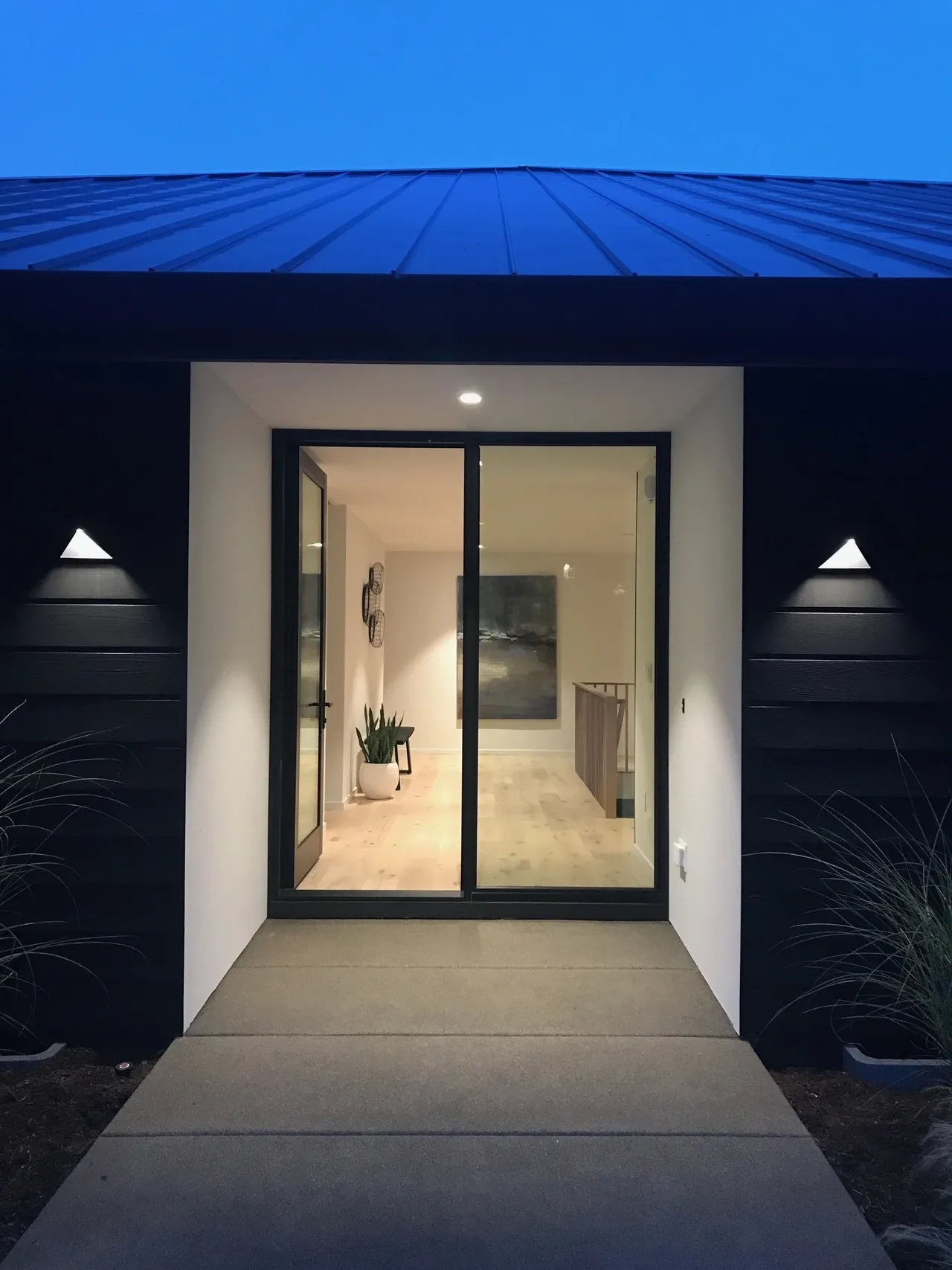 The Cardinal House entrance features a black-framed glass door under a metal roof with symmetrical wall-mounted lights at dusk.