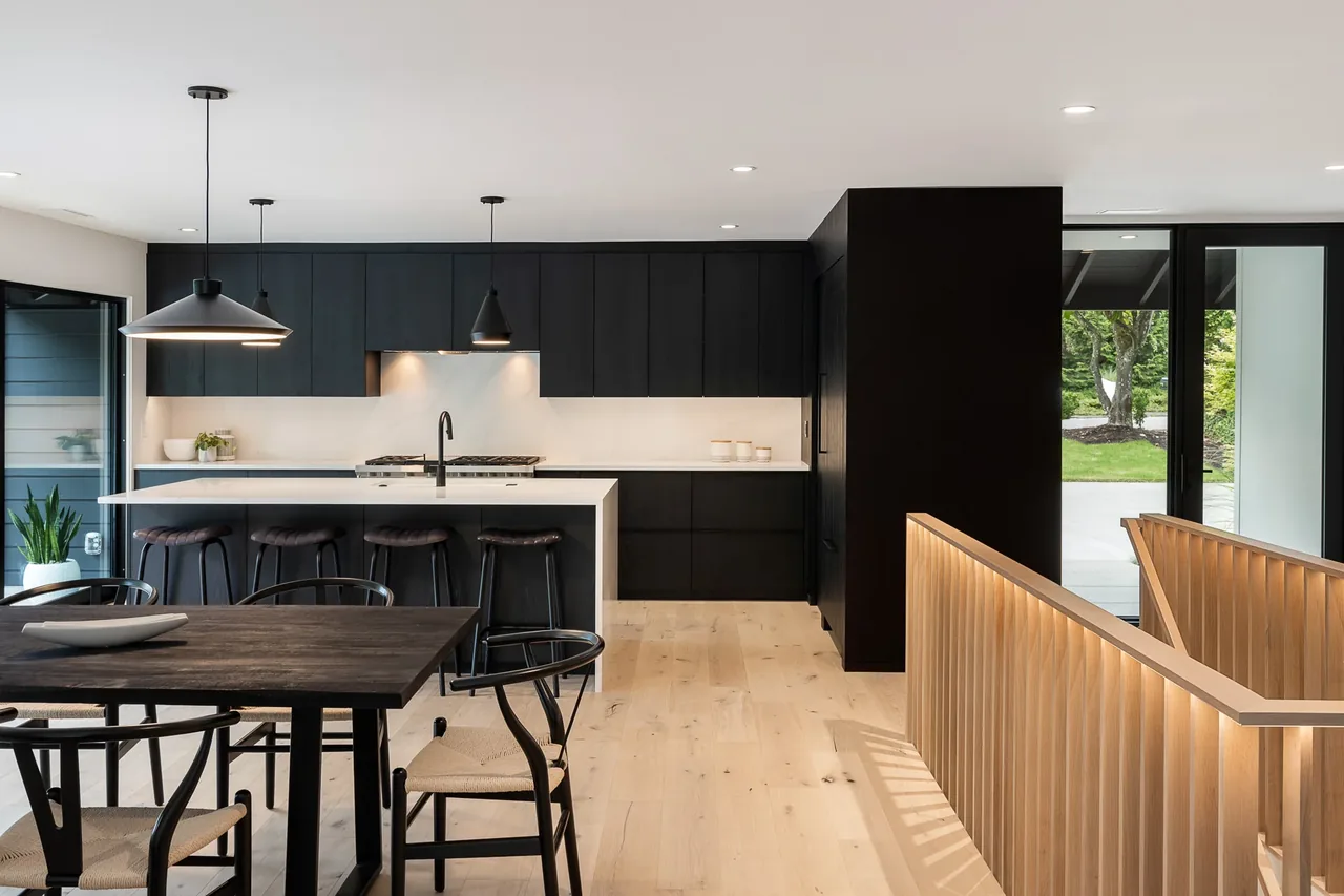 Kitchen in the Cardinal House features black wood cabinets, a white marble island, and large sliding glass doors.