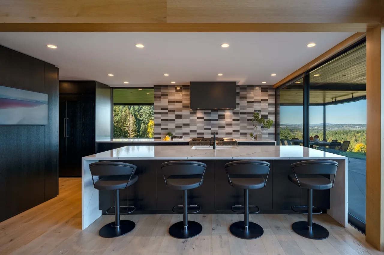 Kitchen with black cabinetry, a white island, geometric tile backsplash, and expansive glass doors opening to outdoor views.
