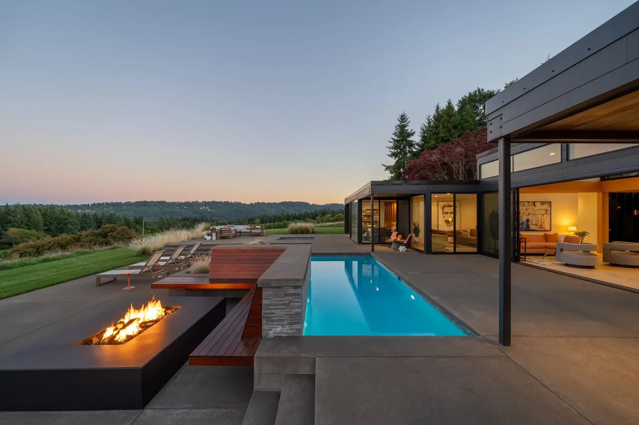 Modern home's outdoor living area includes a rectangular pool and a fire table with seating on a concrete patio.