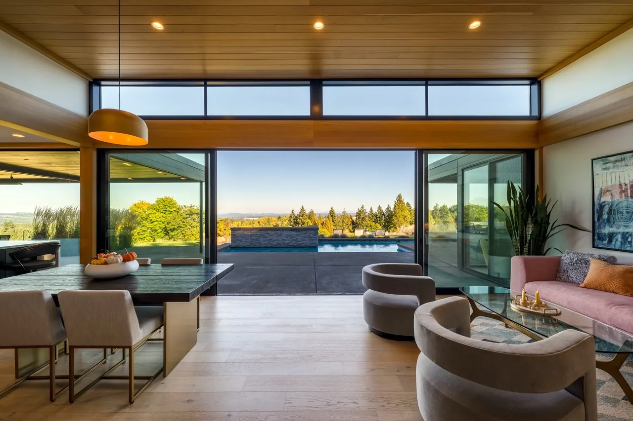 Open living and dining spaces with floor-to-ceiling sliding glass doors connecting to a pool and scenic forest views.
