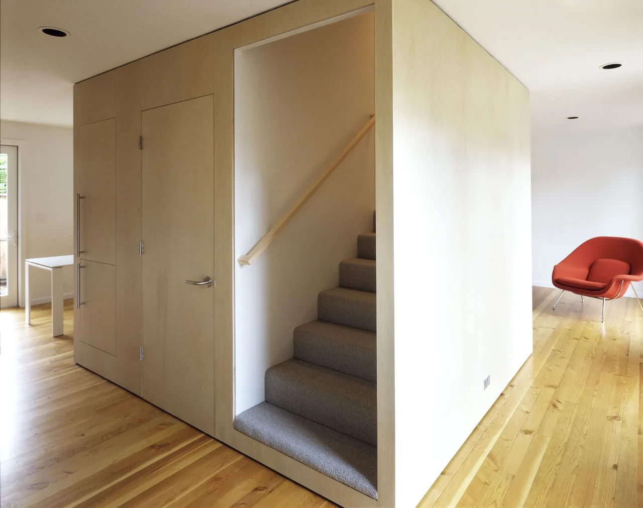 Carpeted stairs enclosed in light wood paneling within a contemporary interior with polished wood floors and recessed lighting.
