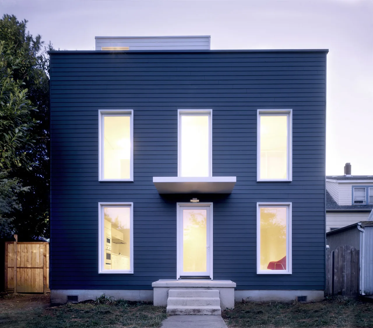 Modern-style front facade of Cape Cod project with blue wood siding and symmetrical window arrangement.