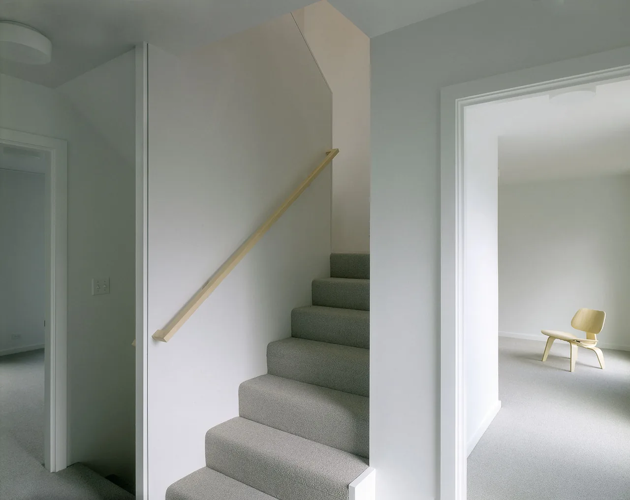 Interior view of a carpeted stairway and adjacent rooms with minimal furniture and white walls.
