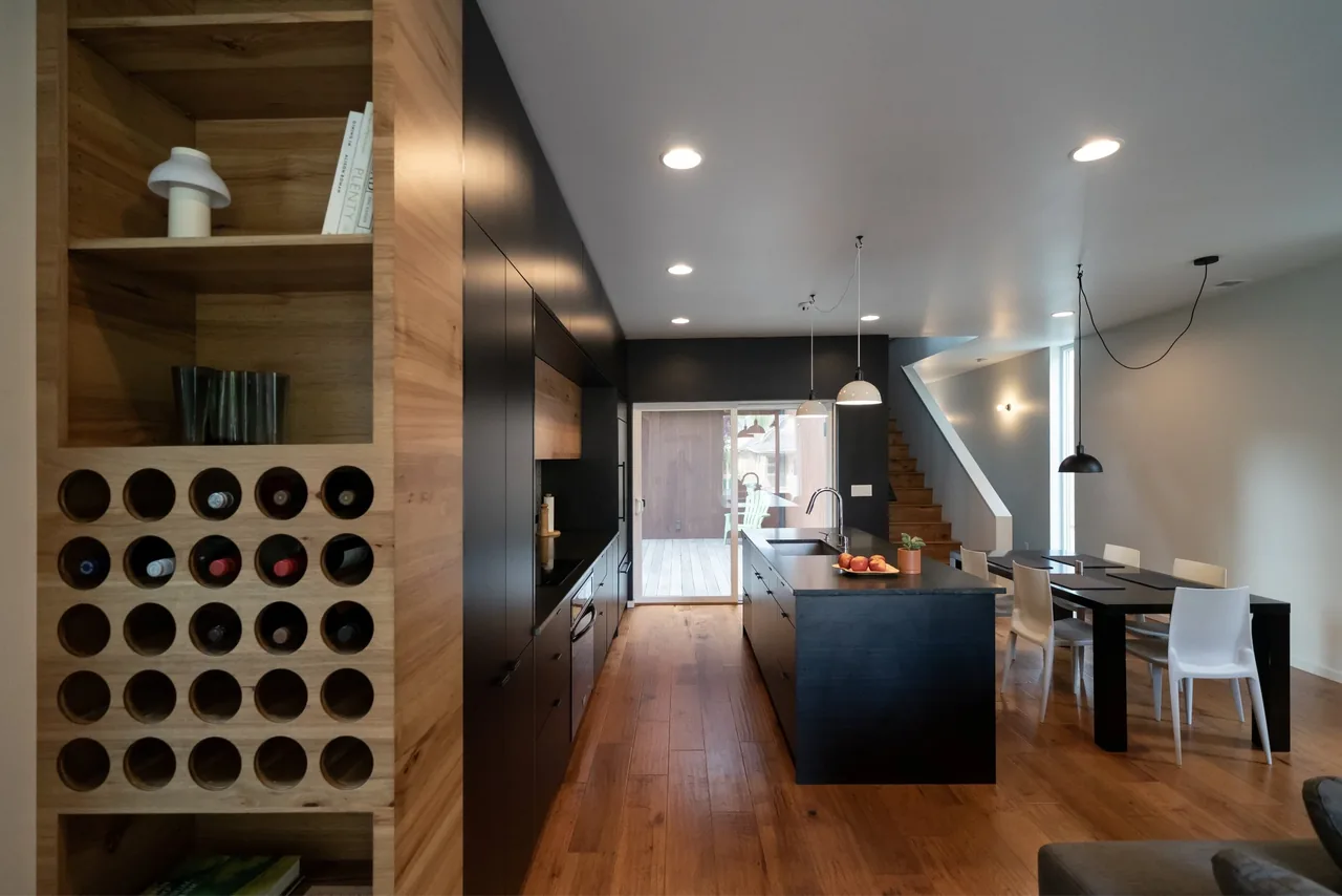 The Cleveland House kitchen features a black island, wood floors, and built-in horizontal wine bottle storage with adjacent dining space.