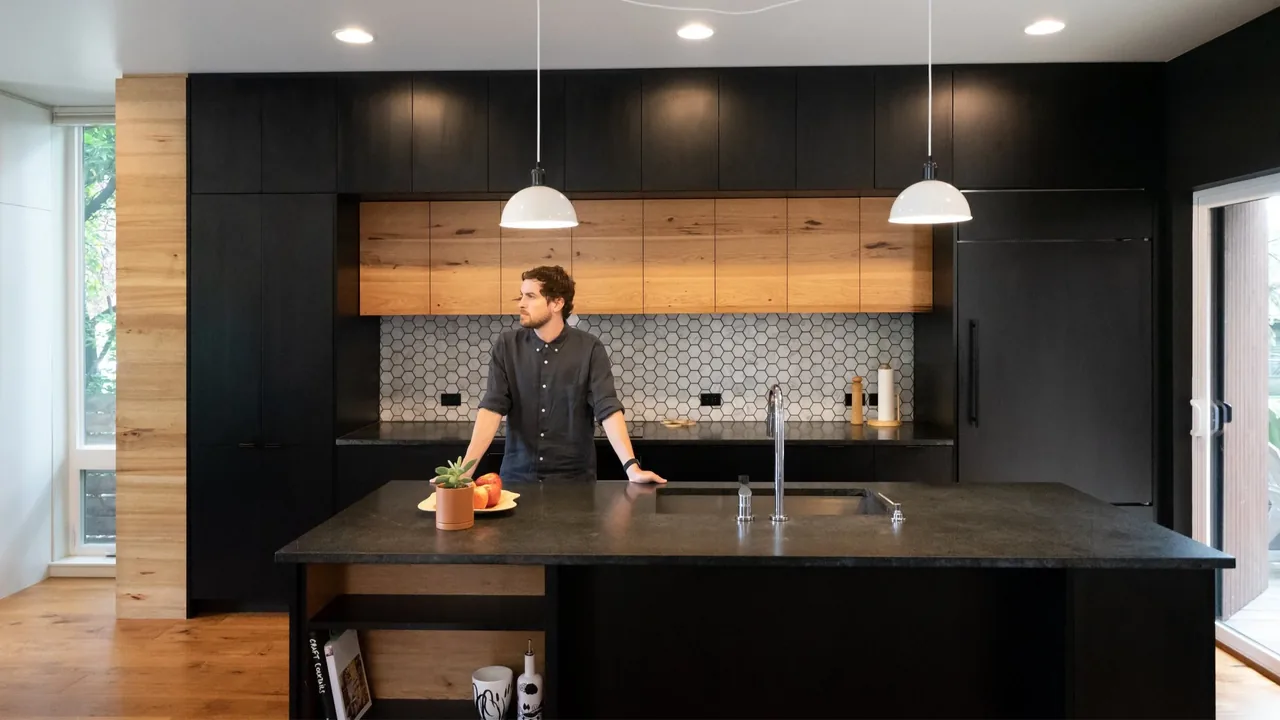 The kitchen features black lower cabinets, wood upper cabinets, hexagonal tile backsplash, and a large island with sink.
