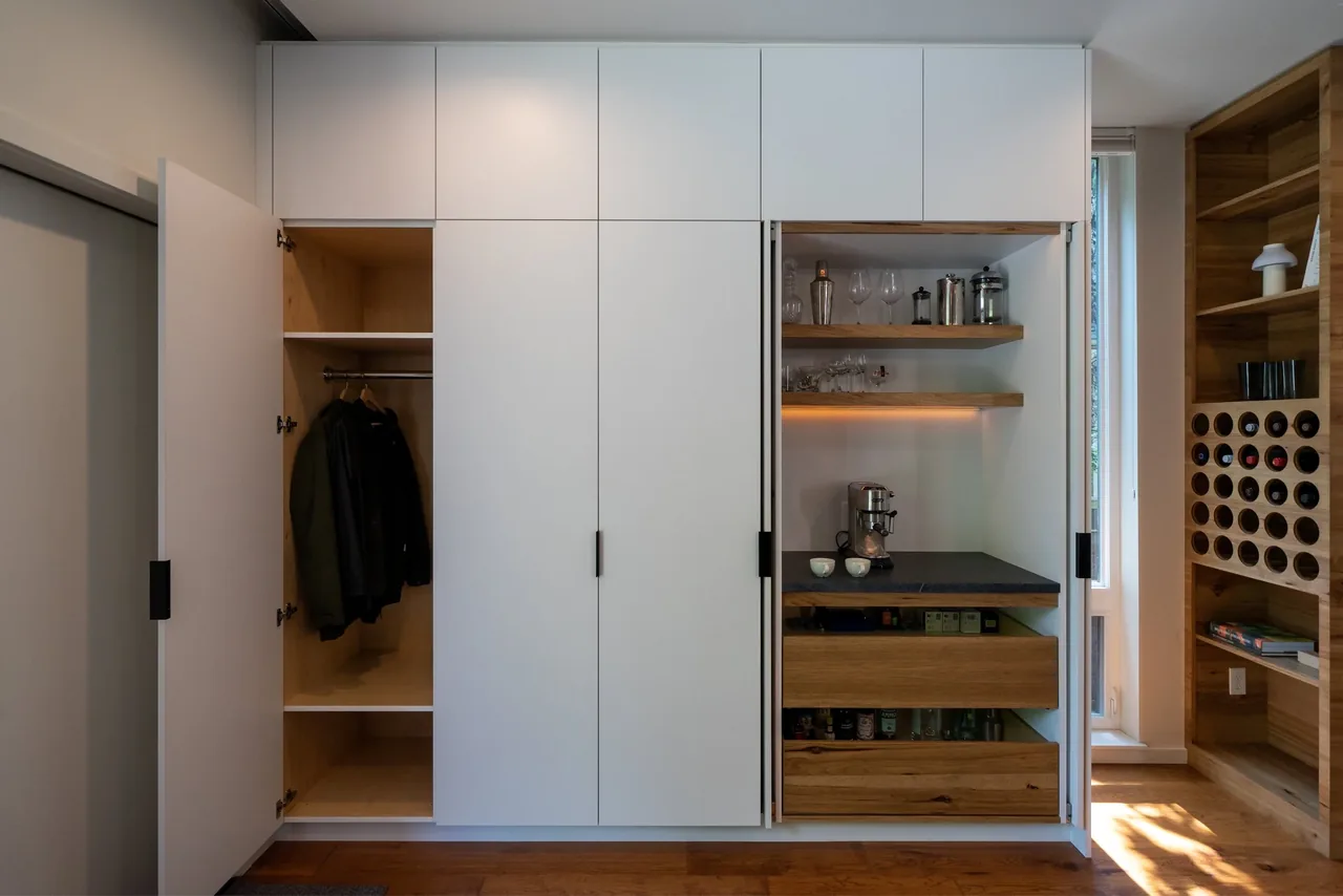 White built-in kitchen cabinetry with vertical black handles includes a coffee station and integrated wine bottle storage.