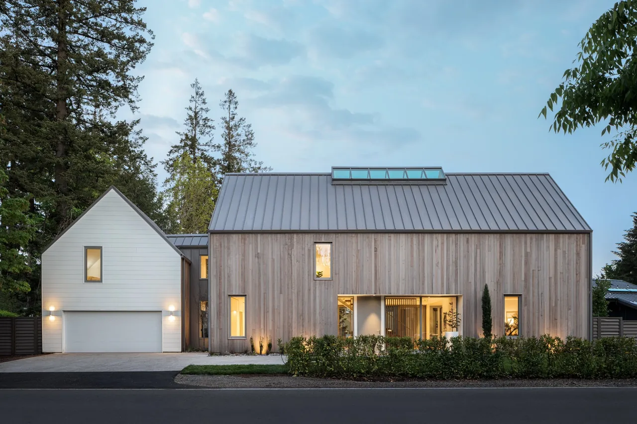 View of a modern two-story house with vertical wood siding and a metal standing seam roof, illuminated at dusk.