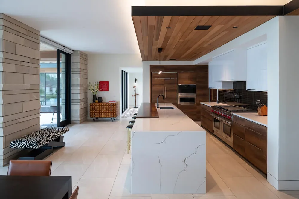 Modern kitchen in Pelican House shows marble island, wood cabinets, and wood ceiling panel by Winn Wittman Architecture.