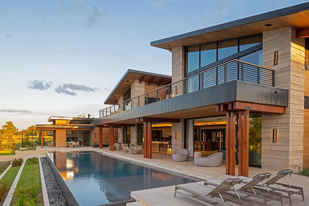 Pelican House features a modern design with stone siding, wood accents, and an outdoor pool with terrace seating.
