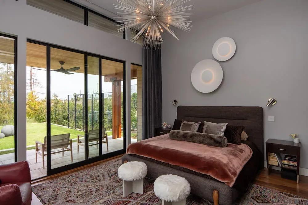 Bright bedroom with sliding glass doors leading to outdoor patio and garden, with decorative ceiling fixture and circular wall lights.
