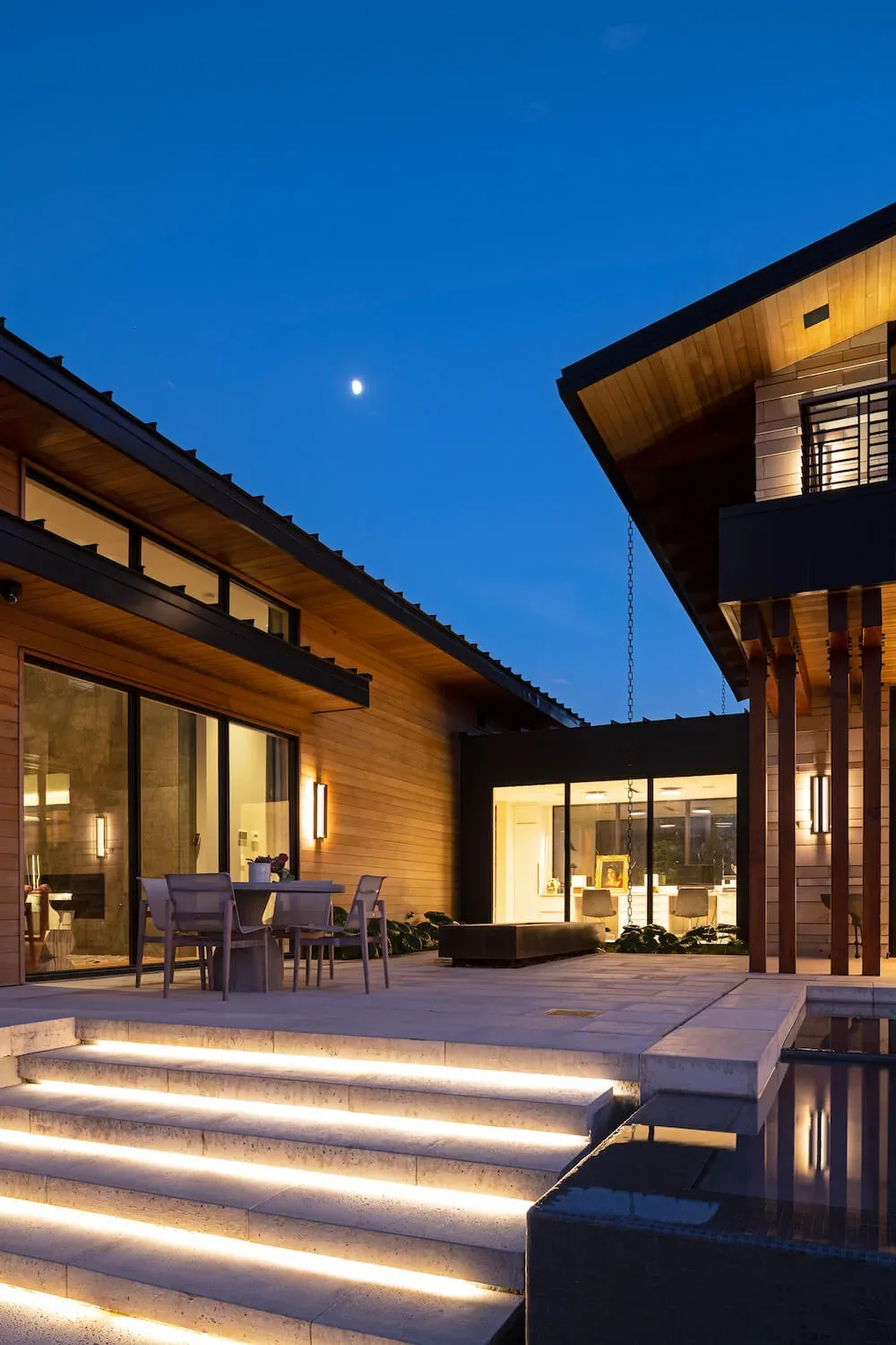 The Pelican House courtyard features wood siding, large glass doors, and illuminated concrete steps at dusk.