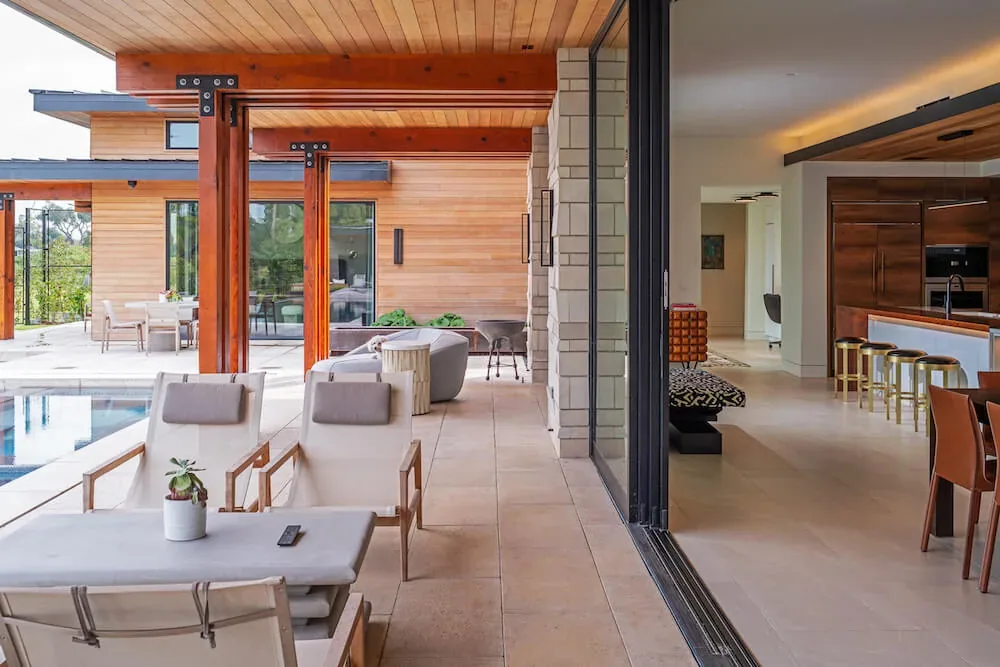 Covered patio space with wood ceiling panels overlooks pool and leads to modern kitchen inside Pelican House.