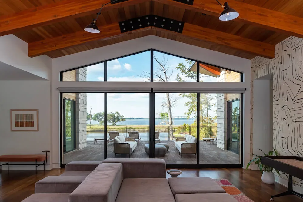 The Pelican House living room features vaulted wood ceiling and floor-to-ceiling sliding glass doors to an outdoor deck with waterfront views.