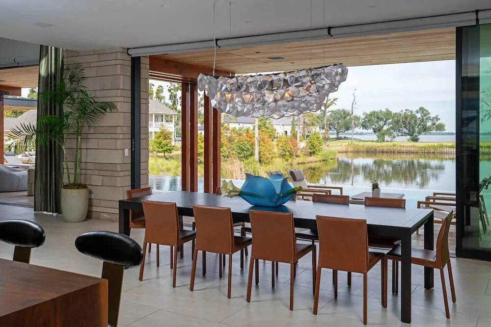 Dining space featuring leather chairs around a dark table with a sculptural pendant light and expansive sliding glass doors opening to water views.
