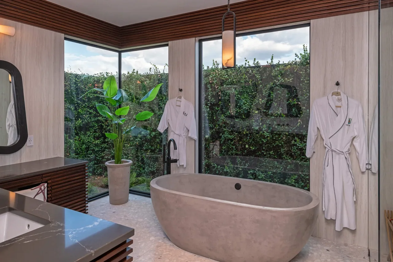 Pelican House bathroom with a freestanding tub and large corner windows providing a lush outdoor view.