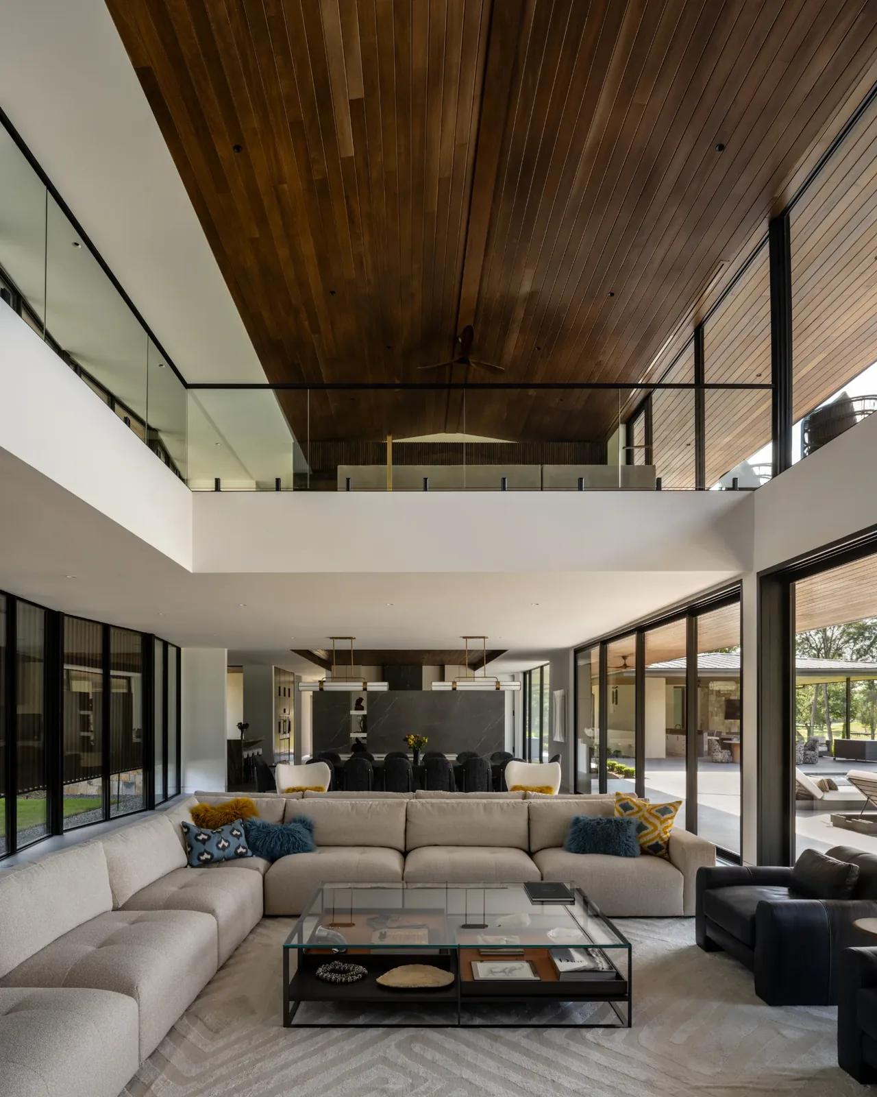 Spacious open-plan living room with a high wood-paneled ceiling and balcony overlooking the seating area.