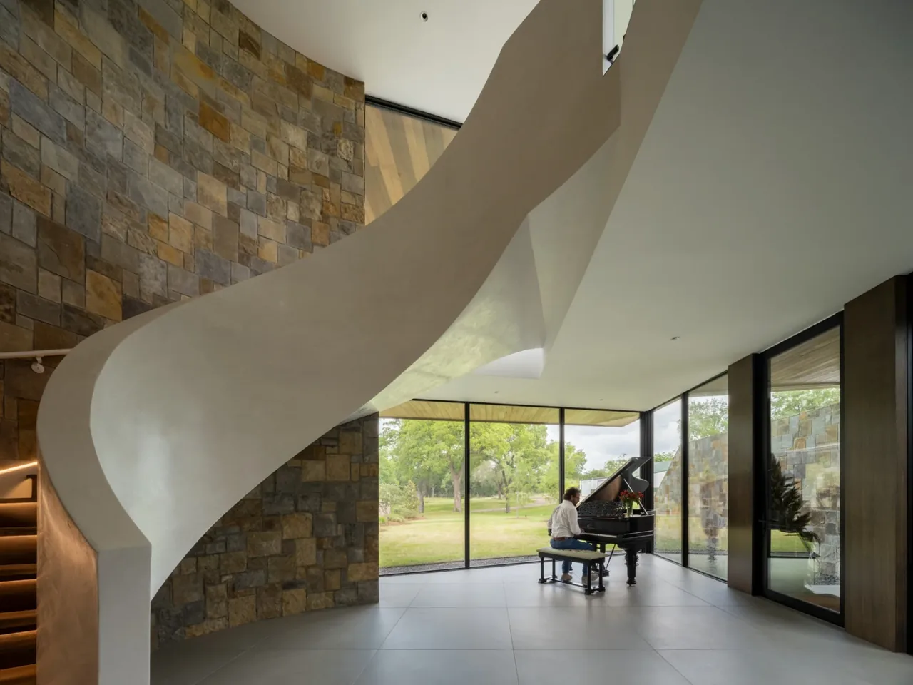 Interior space features a curved stucco staircase, floor-to-ceiling glazing, and a grand piano.
