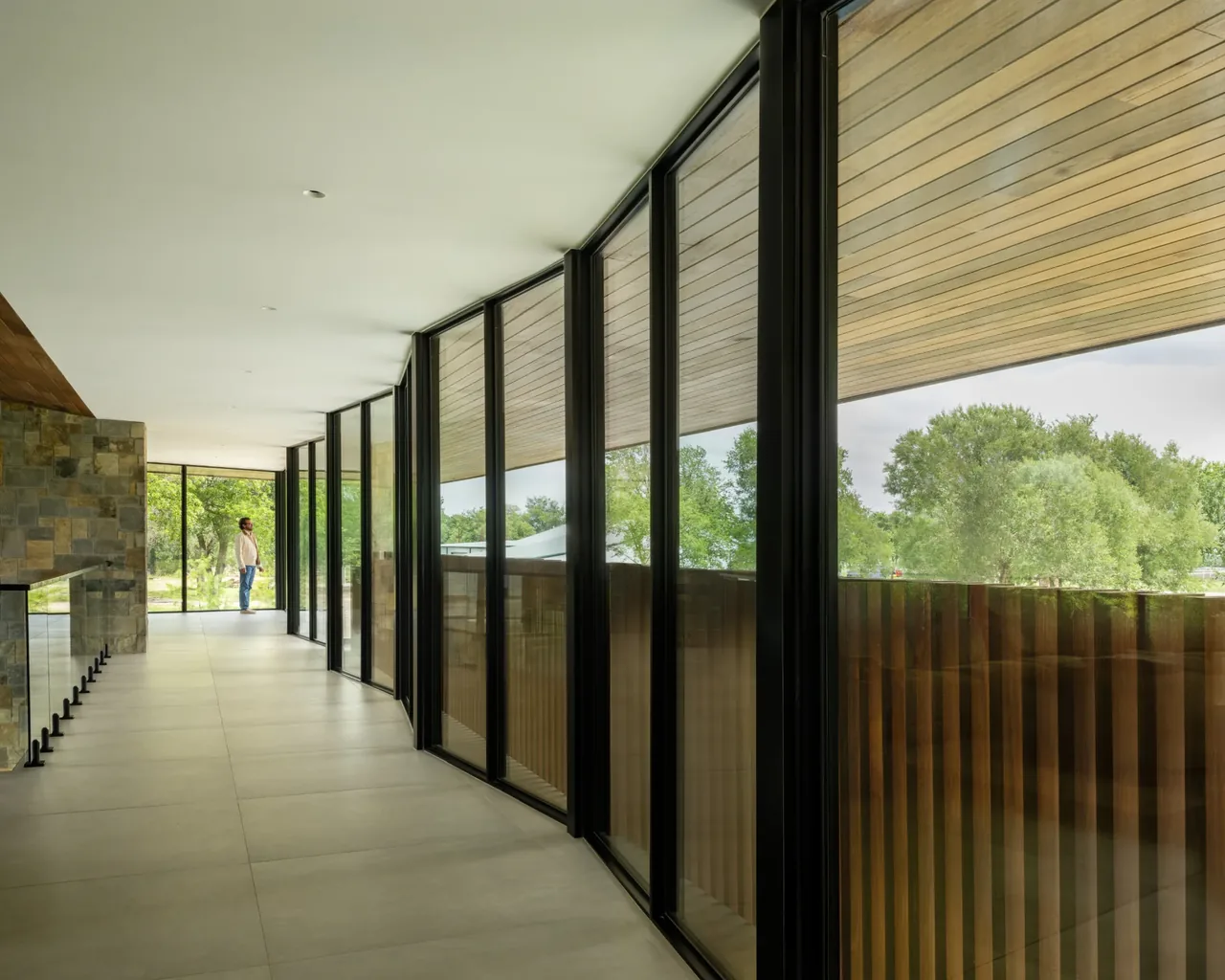 Hallway with floor-to-ceiling glass windows and stone accent wall in the Horse Ranch project by Winn Wittman Architecture.