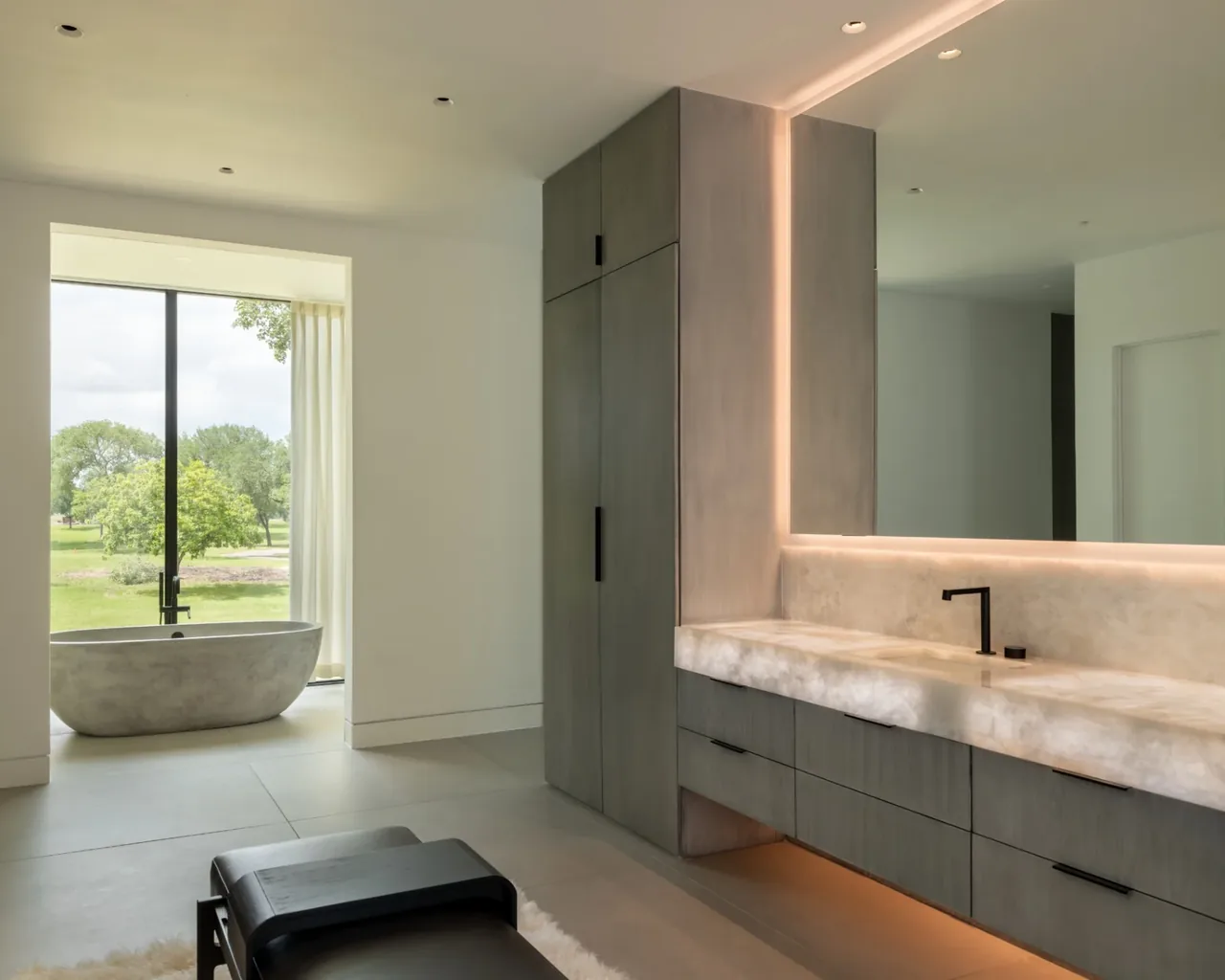 Bathroom with a freestanding stone bathtub by the window and a long stone vanity with black faucet and handle accents.