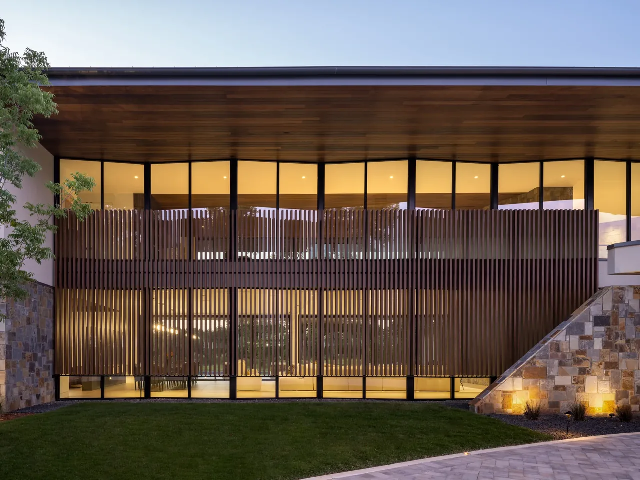 The Horse Ranch features a modern glass facade with vertical wooden slats and illuminated landscape lighting beneath a wide roof.
