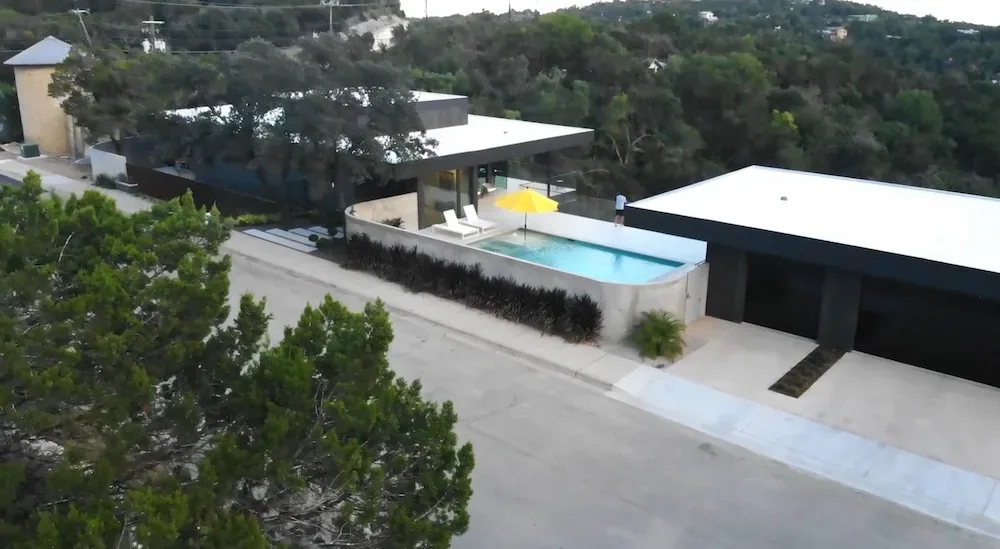 Villa Morada features flat roofs, an elevated pool with seating, and modern minimalist architecture on a wooded hillside.