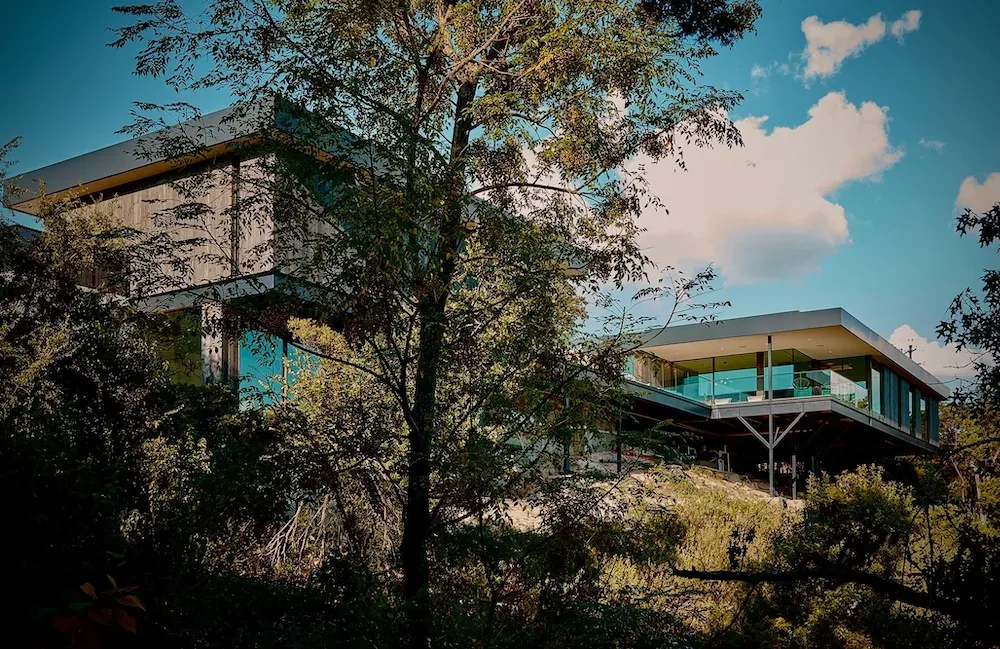 Villa Morada features a modern design with multiple roof peaks and a glass pool fence, set amidst natural greenery in Austin.