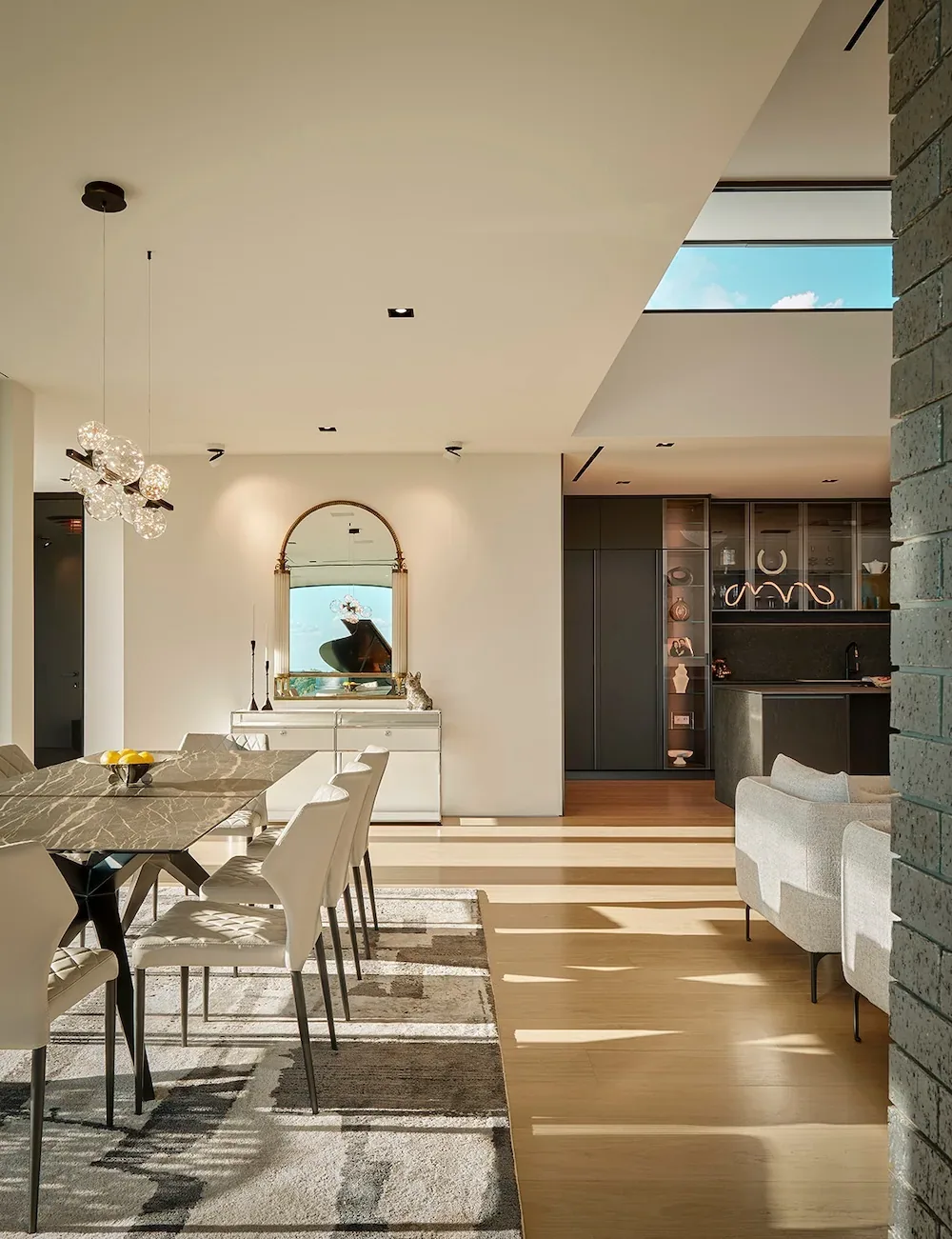 Open dining area with marble table and chandelier, adjacent to living space with light color scheme and natural light.