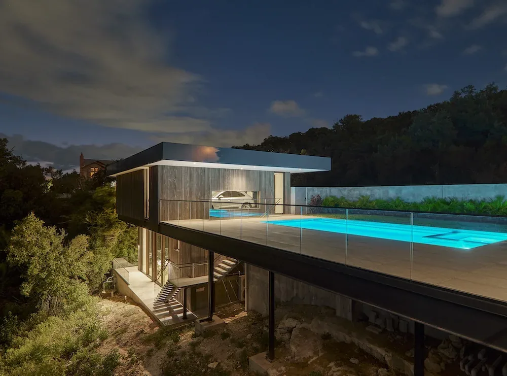 Villa Morada features a modern design with an elevated outdoor pool deck surrounded by a glass fence, highlighted in evening light.