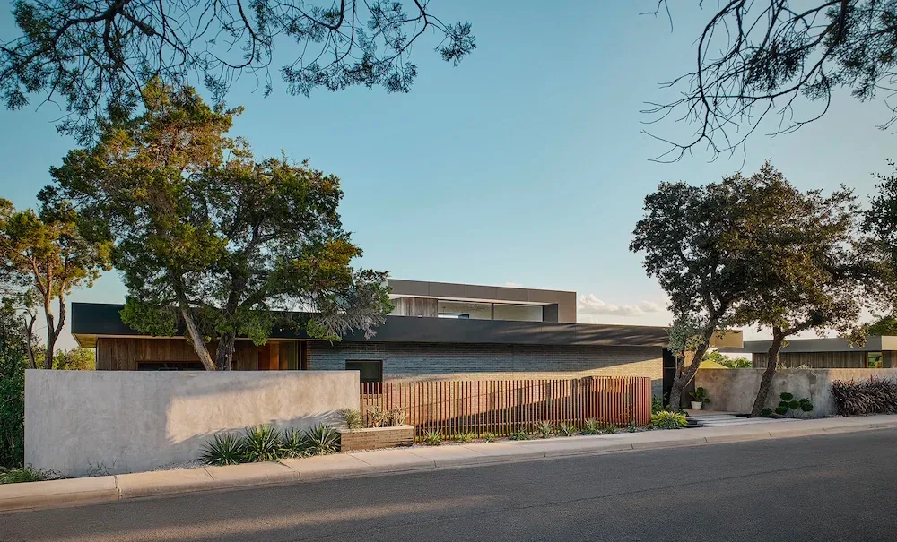 Villa Morada features a modern design with multiple roof peaks and a mixed material facade behind a concrete and wood slat fence.