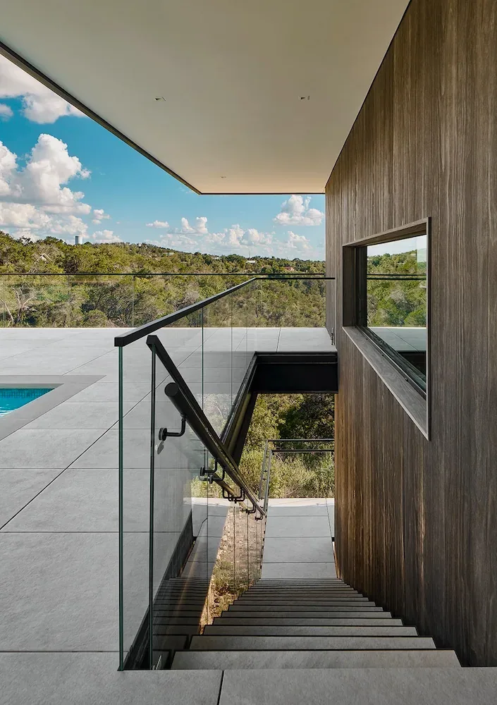 Glass-railed outdoor staircase next to a wood-clad wall at Villa Morada with views of surrounding greenery.