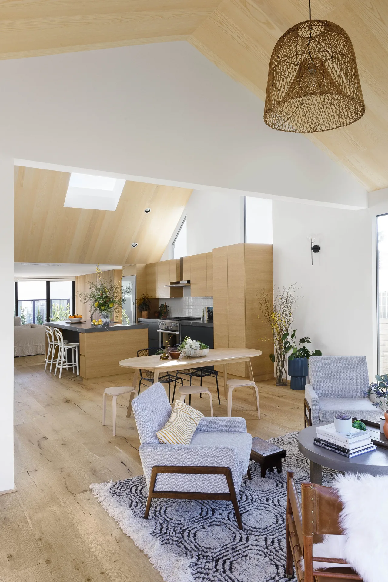 Open-plan living and kitchen area featuring vaulted ceilings, wood cabinetry, and woven pendant lighting.