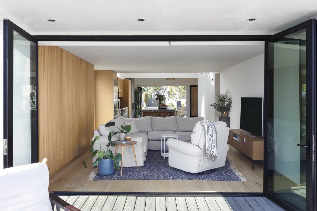Curson Residence living room with black sliding glass doors and light wood flooring, showing the open layout toward the kitchen.