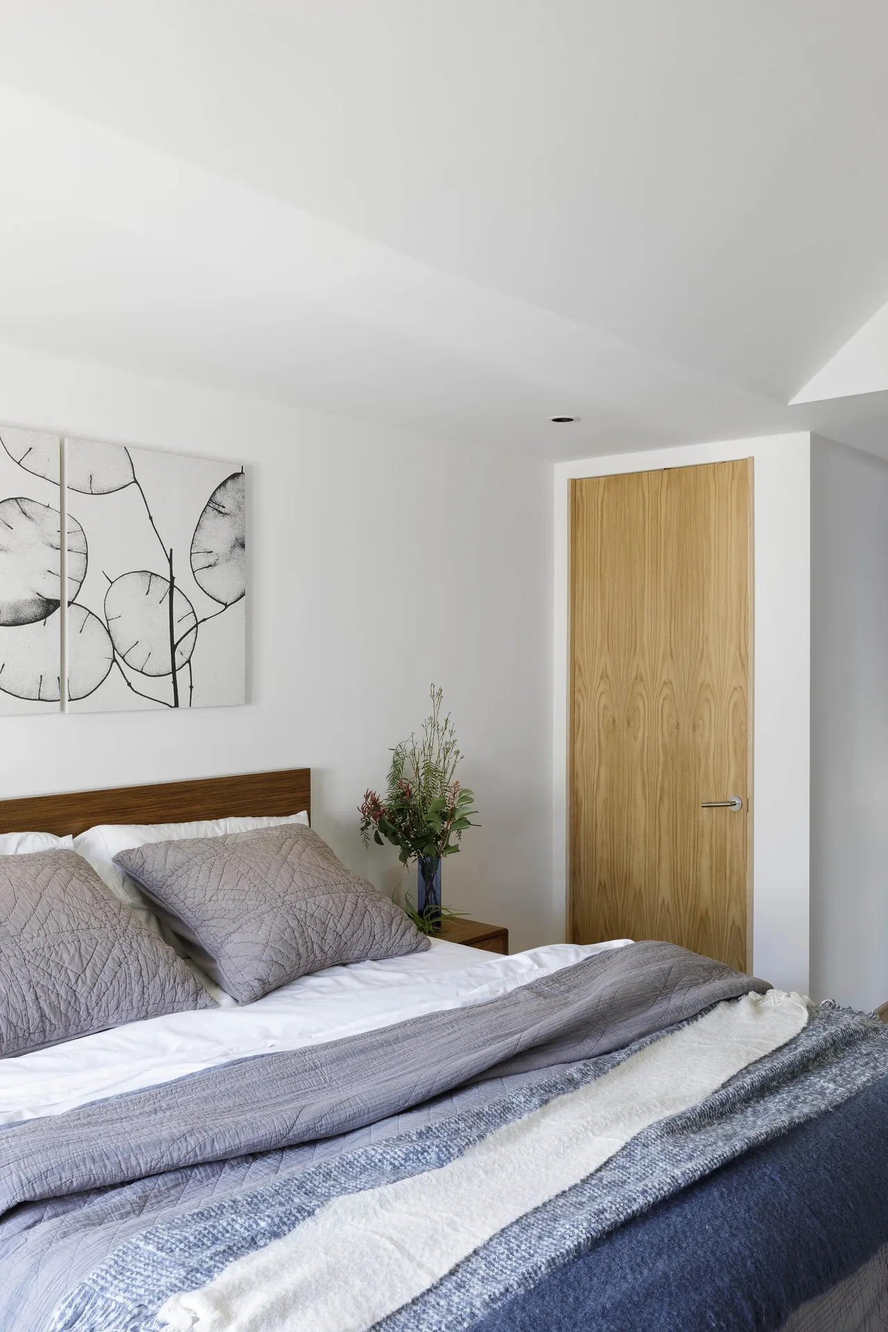 Curson Residence bedroom with wooden headboard, gray quilted bedding, and a light wood door by Nwankpa Design.