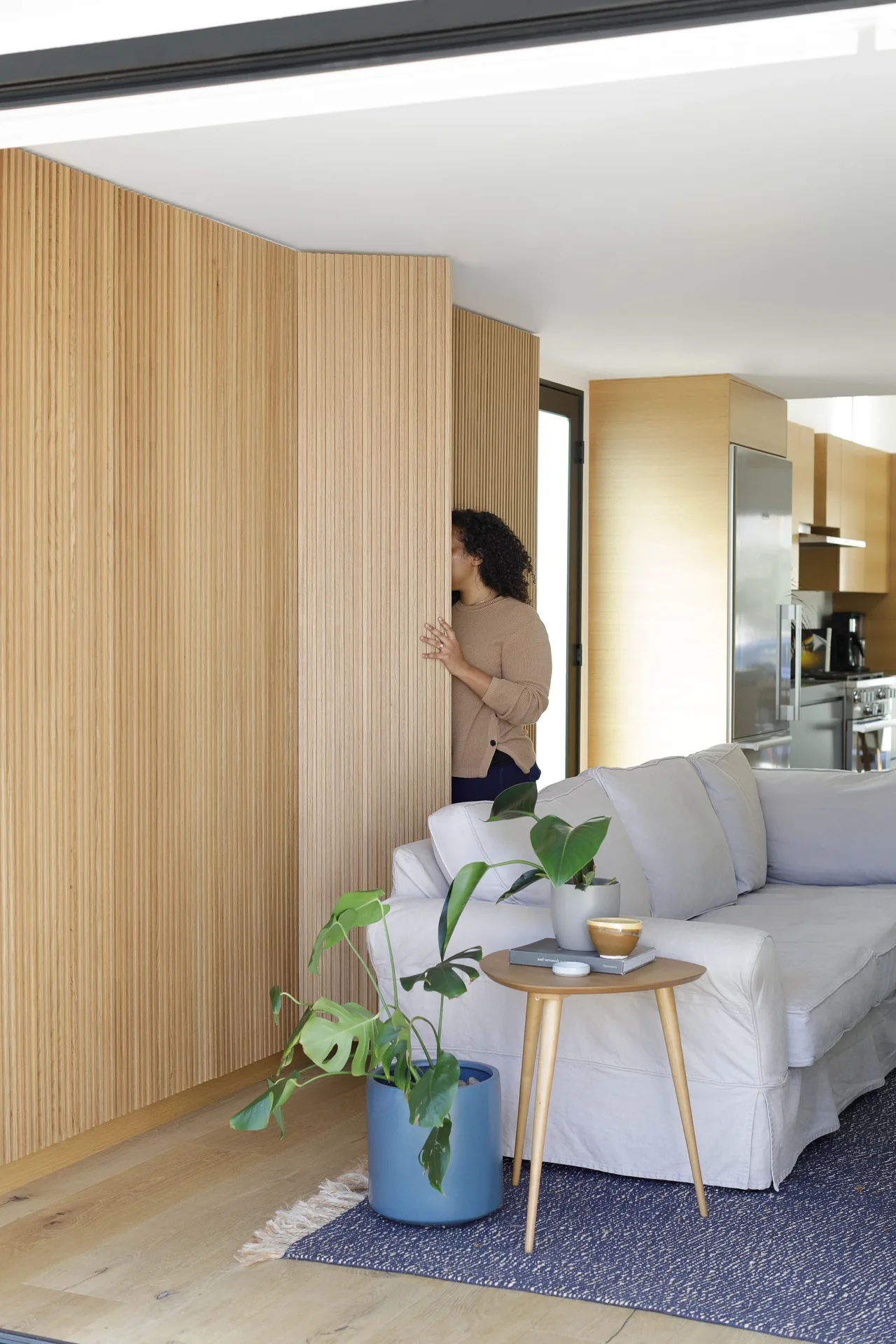 The Curson Residence features wood-paneled walls and an open living area with blue area rug and light wood flooring.