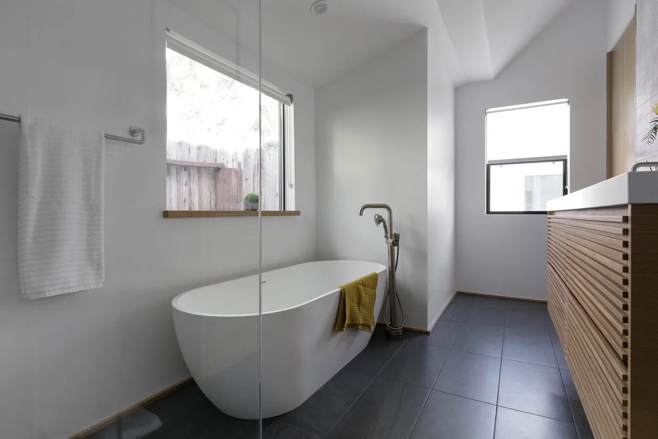 The Curson Residence bathroom features a freestanding tub with a floor-mounted faucet and a wood-paneled vanity.