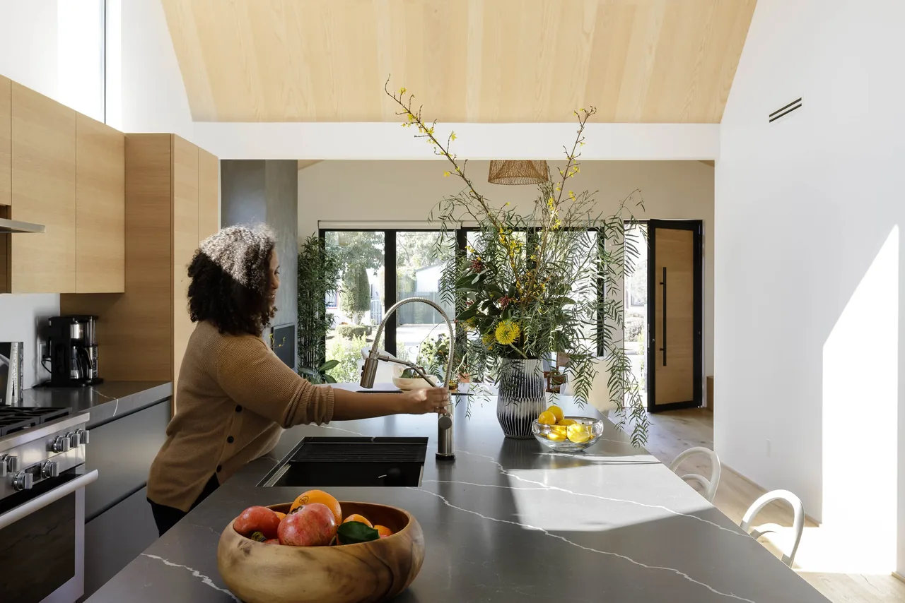 The kitchen features a wood-paneled ceiling, a large marble island with integrated sink, and light wood cabinetry.