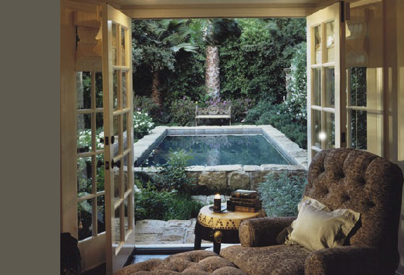 Living room opens through French doors to a garden with a raised pool and lush plants.